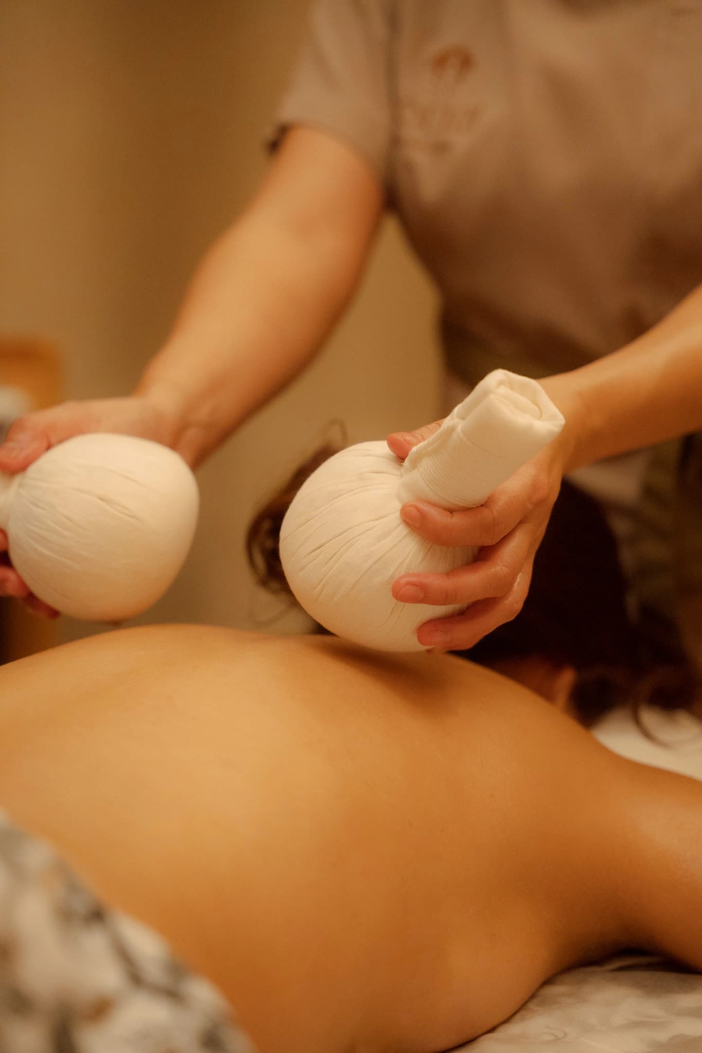 Two warm Thai herbal compresses held above a guest's back