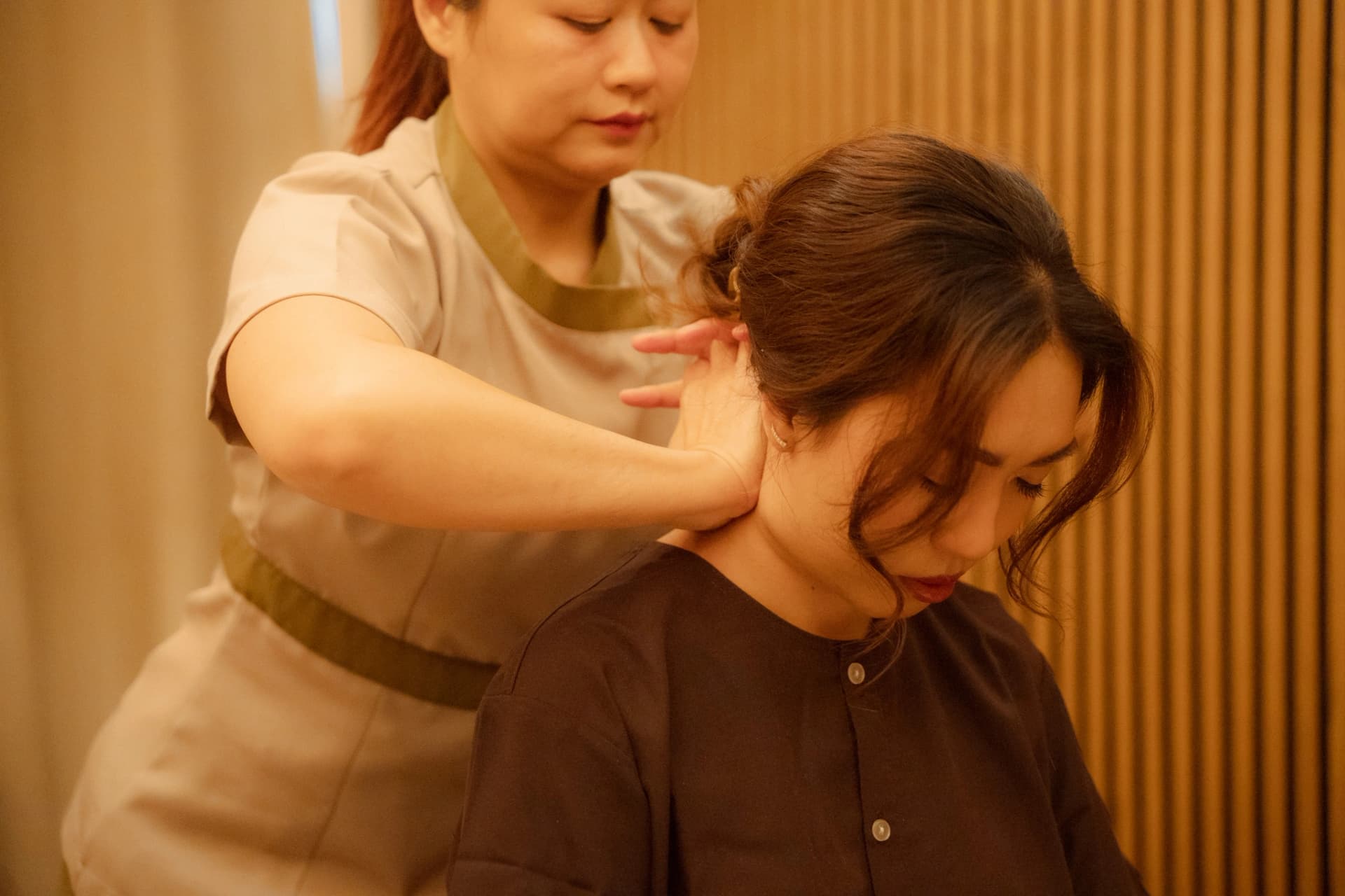 A therapist working on a seated guest's neck and shoulder